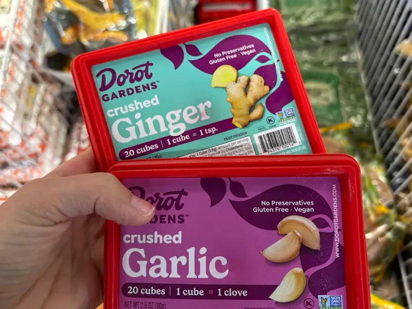 A hand holding boxes of crushed garlic and crushed ginger.