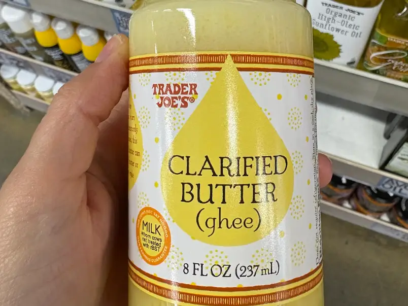 A hand holding a jar of clarified butter, or ghee.